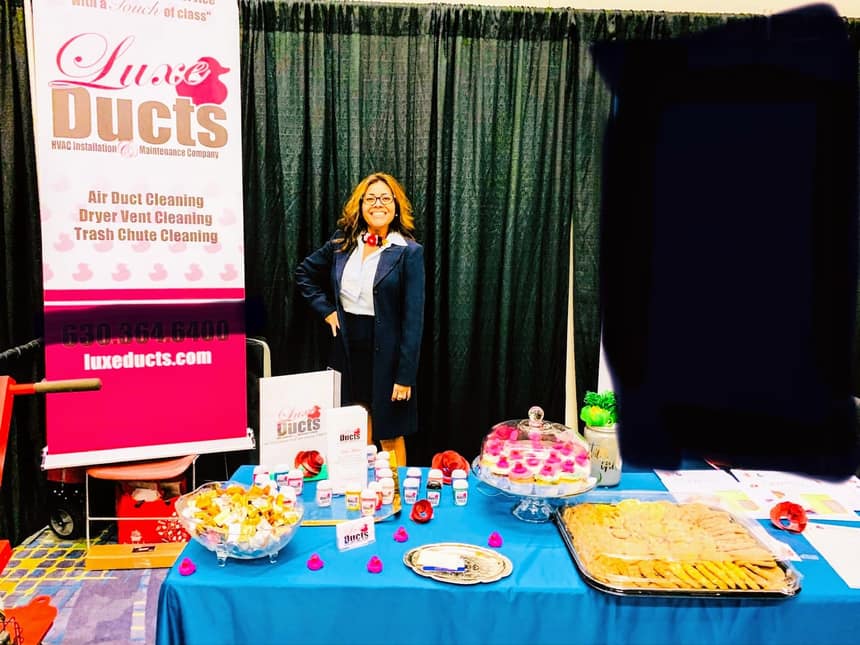 Connie Luce at the Luxe Ducts booth at a Chicagoland business expo, pink banner behind her
