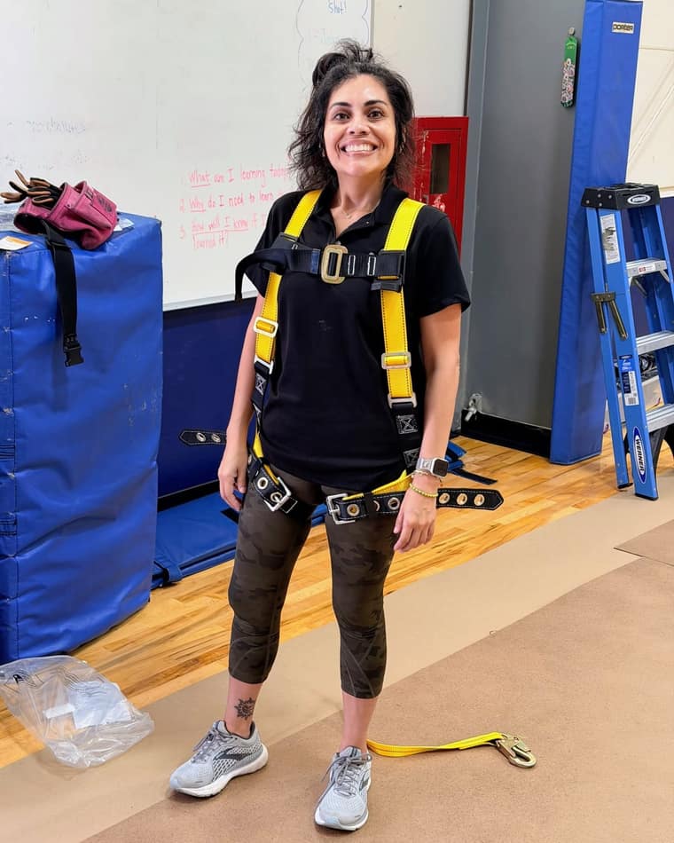 Connie Luce in a Luxe Ducts polo and a full body fall arrest harness before an elevated access job in a school gym