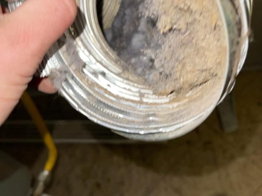 A gloved hand holding a cut length of dryer duct with the lint still packed inside it