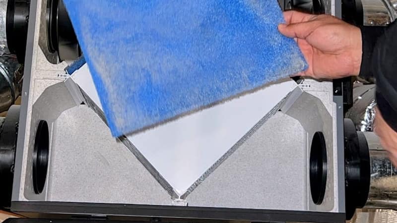 A Luxe Ducts technician lifting a blue filter media pad out of an air handler cabinet