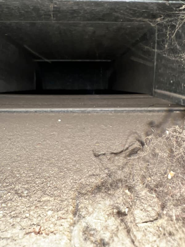 Looking down the inside of a rectangular sheet metal duct run, the floor of it covered in dust and debris